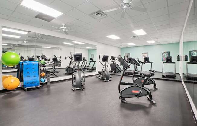A gym with a variety of exercise equipment including treadmills, stationary bikes, and weights.