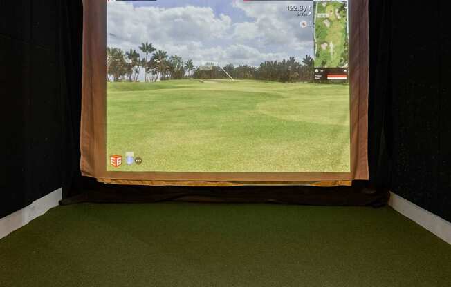 A golf course is displayed on a screen in a dark room.
