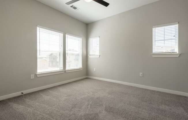 an empty living room with three windows and a ceiling fan