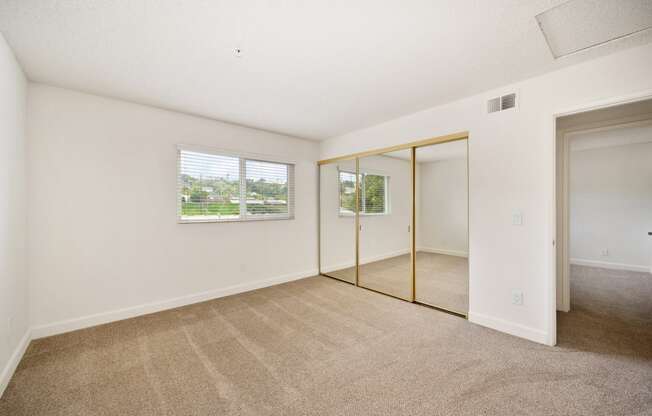 the living room of an apartment with carpet and mirrored doors