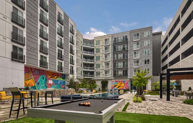 A pool table is in the middle of a grassy area surrounded by buildings.
