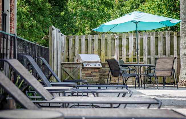 A row of lounge chairs are arranged in front of a wooden fence and a green umbrella.
