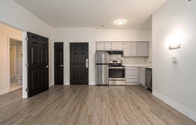 an empty living room and kitchen with black doors and stainless steel appliances