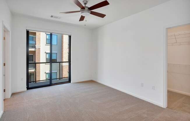 an empty living room with a large window and a ceiling fan