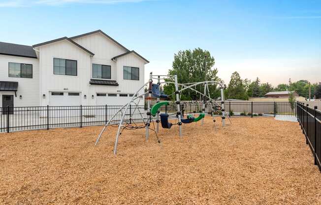 A playground with a swing set and a slide in front of a white house.