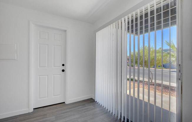 A white door with a black handle is in a room with a window covered with white blinds.