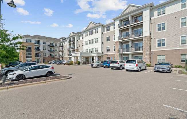 A parking lot in front of apartment buildings with cars parked.