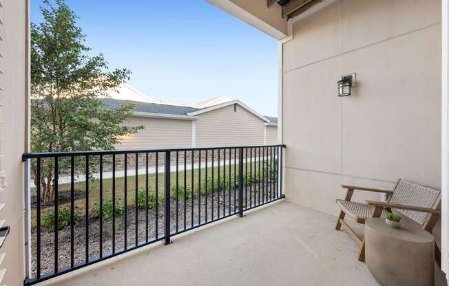 A balcony with a black railing, a chair, and a table with a plant on it.