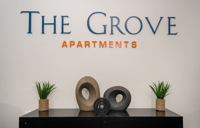 A black table with three decorative objects on it in front of a wall with the text "The Grove Apartments" written on it.