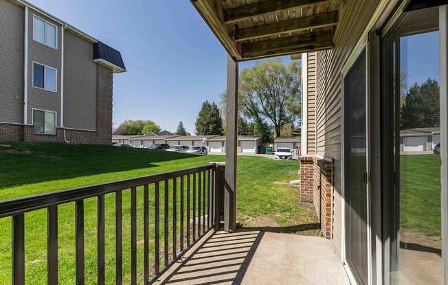 A balcony with a black railing and a view of a grassy area and other buildings.