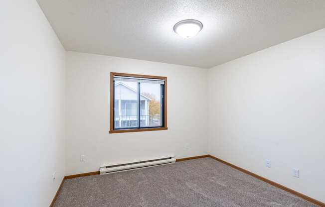 an empty living room with carpet and a window. Fargo, ND Flagstone Apartments