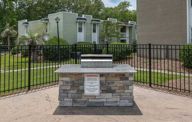 A warning sign is on a stone pillar in front of a black fence.