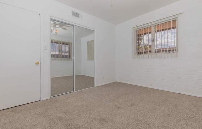 A room with a carpeted floor, a window with blinds, and a sliding glass door.