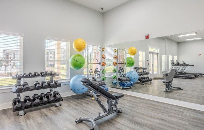 a gym with exercise equipment and weights on the floor and a large window
