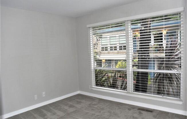 an empty living room with a large window with blinds