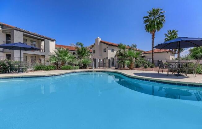 A swimming pool surrounded by palm trees and a building in the background.
