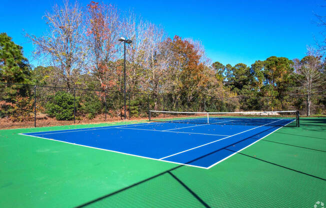 a tennis court with blue and green turf and a fence