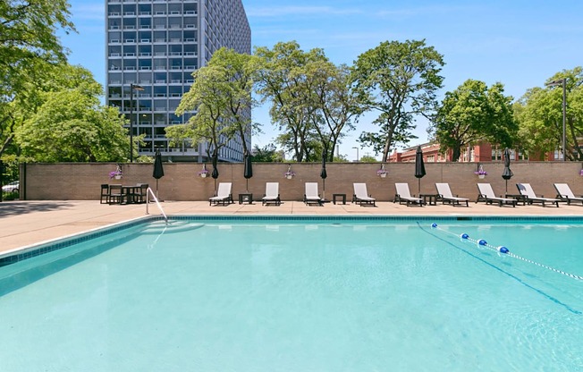 A swimming pool surrounded by trees and chairs.