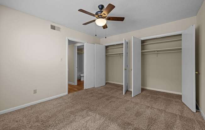 an empty living room with a ceiling fan and two closets