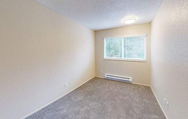Comfortable bedroom at Peak 88 Apartments in Renton WA featuring soft carpeting, neutral tones, and a large window.