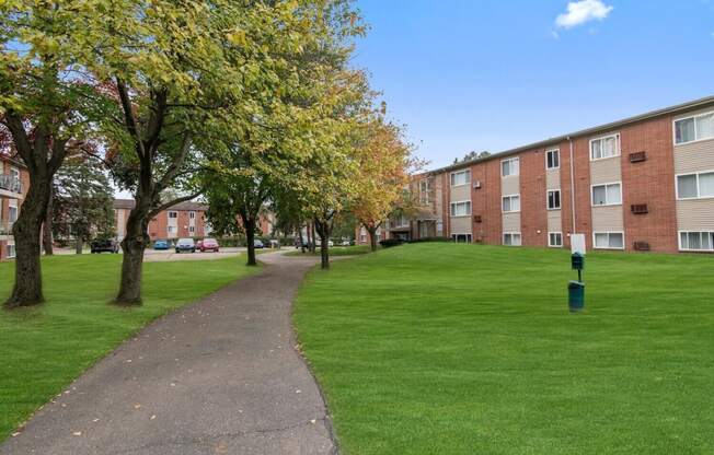 a walkway through a green lawn in front of an apartment building