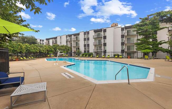 A swimming pool surrounded by a concrete patio and apartment buildings.