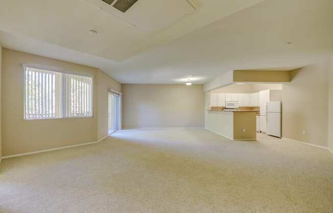 an empty living room with a kitchen in the background