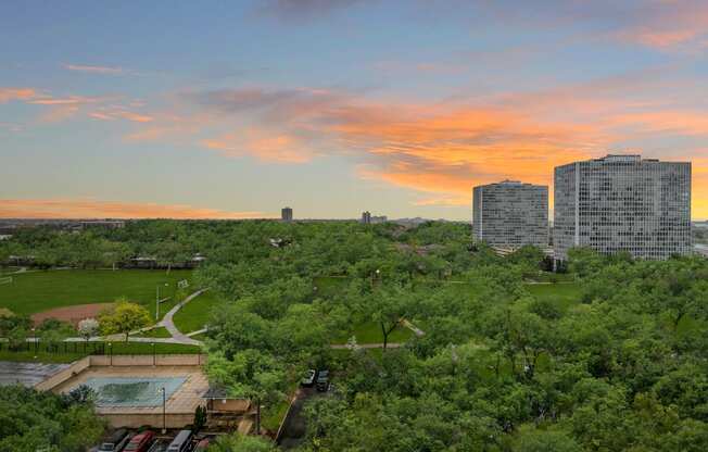 an aerial view of a park with buildings in the background and a colorful sunset in the sky