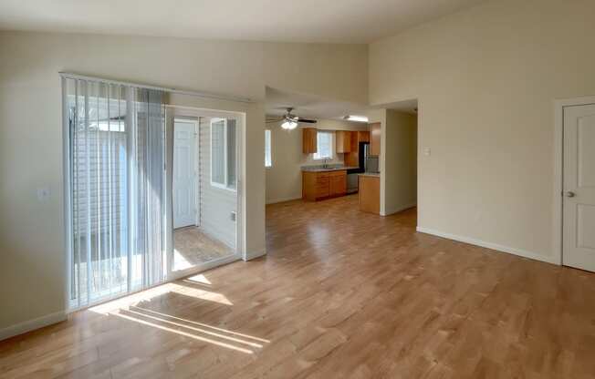 an empty living room with a sliding glass door and a kitchen in the background