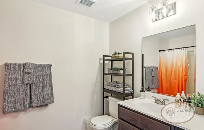 A bathroom with a toilet, sink, mirror, and a hanging coat.