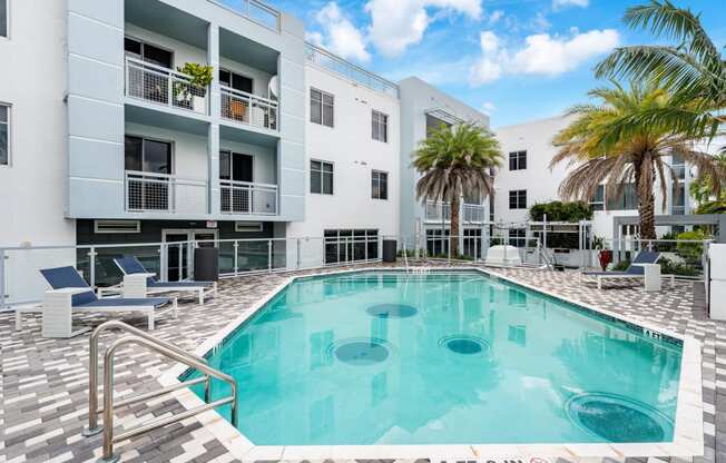 a swimming pool in front of a white building with palm trees