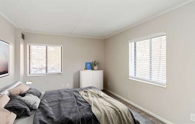 A bedroom with a bed, a nightstand, and a window with blinds.
