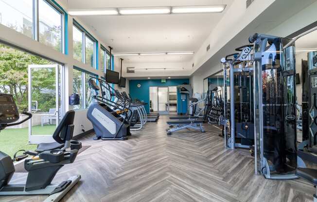 a gym with cardio machines and weights in a building with large windows