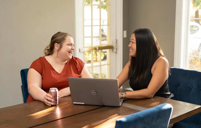 two women sitting at a table with a laptop