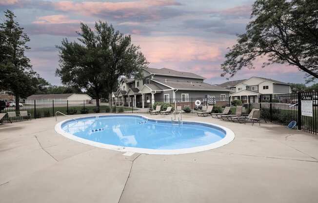 A large outdoor swimming pool surrounded by a fence and a house in the background.