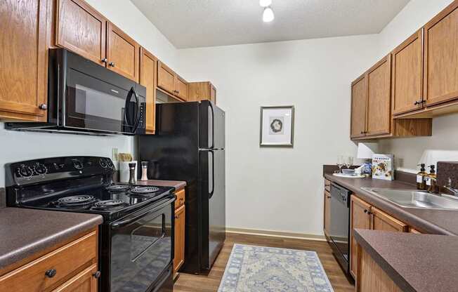 Fully equipped kitchen with black appliances and wood cabinetry in Tattersall Village Apartments, Hinesville, GA