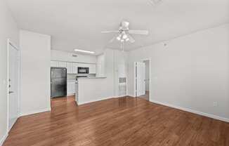 the living room and kitchen of an apartment with wood flooring and a ceiling fan