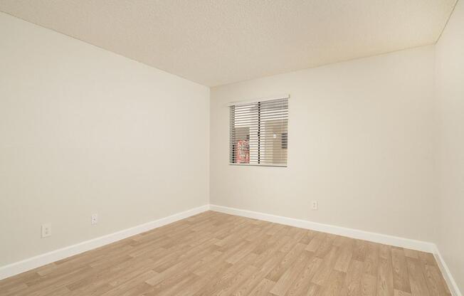 A room with wooden flooring and a window with blinds.
