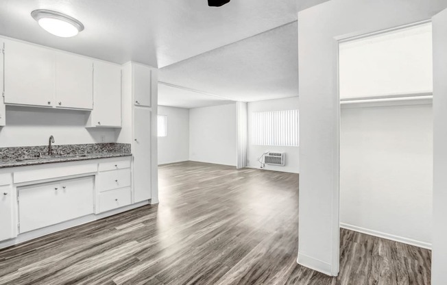 an empty living room and kitchen with white cabinets and wood flooring