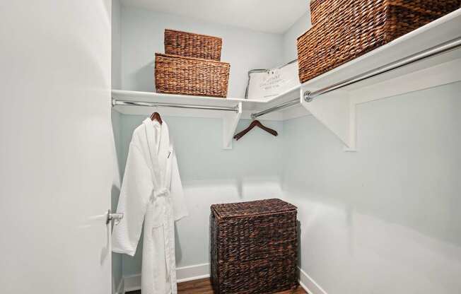 A white bathroom with a white robe hanging on the door and a brown basket on the floor.