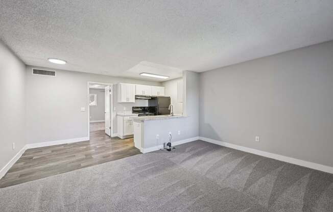 Model living/family room with a gray carpet and a white fridge.