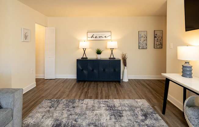 A living room with a grey rug, a white table, a black cabinet, and a lamp.