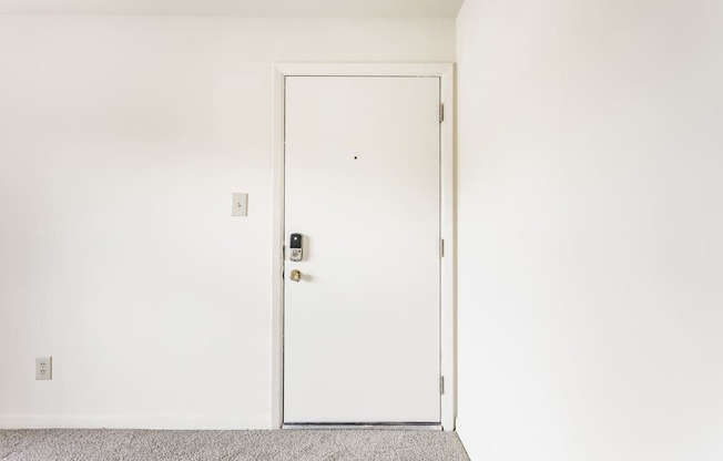 A white door with a handle and a keypad is in a room with a grey carpet