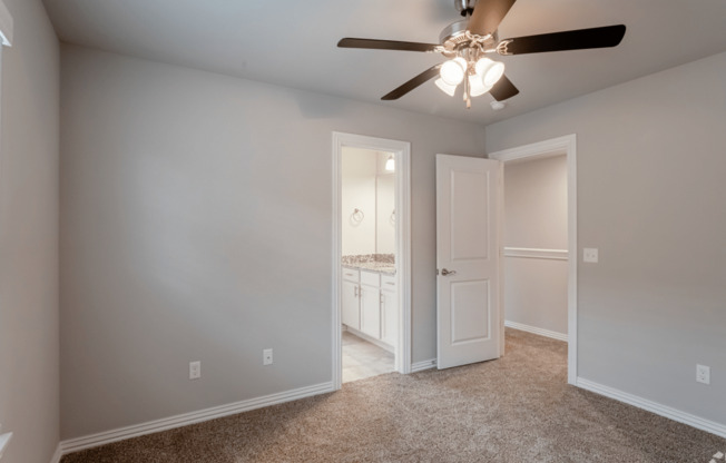 a bedroom with a ceiling fan and a door to a bathroom