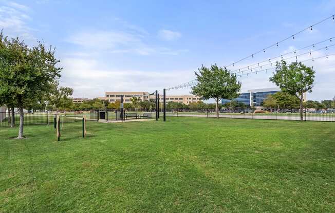 A grassy field with trees and a fence in the foreground and a building in the background.