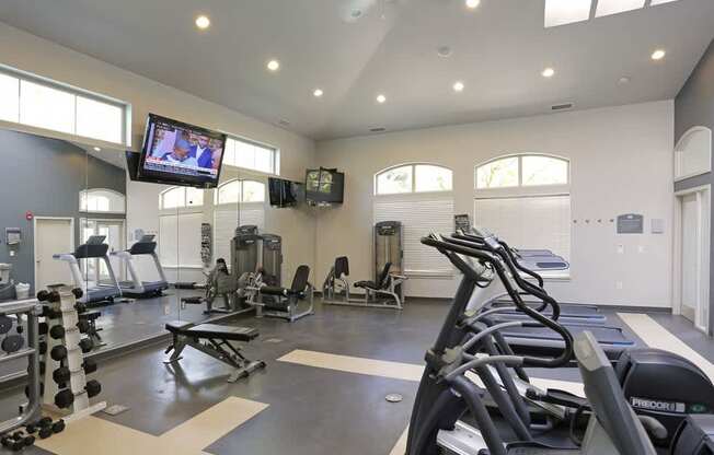 A gym with a row of treadmills and a television mounted on the wall at Wilsonville Summit Apartments, Wilsonville 