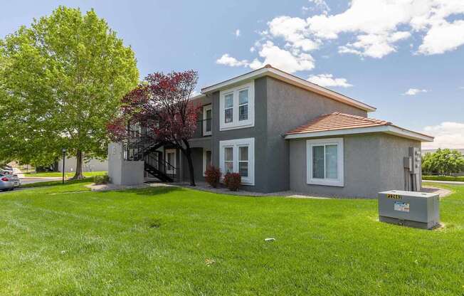 A grey house with a red roof and a green lawn.