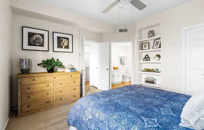 A bedroom with a blue bedspread and a wooden dresser.