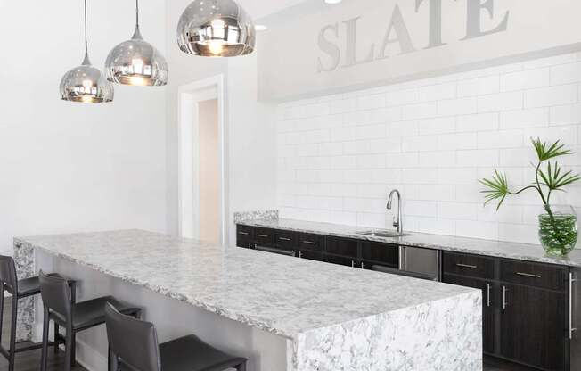 A kitchen with a marble countertop and pendant lights.