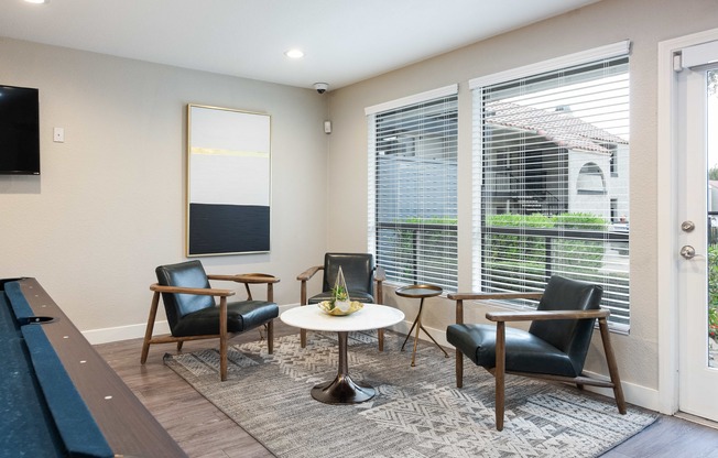 a living room with chairs and a table and large windows